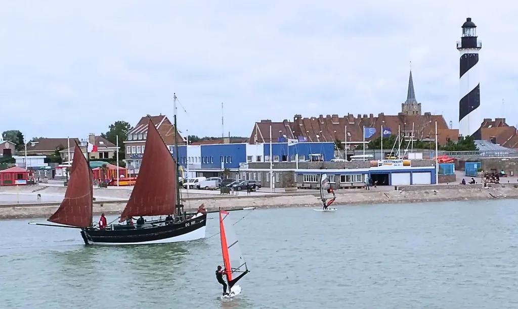 Perspective depuis le gîte BouteilleAlamer sur le chenal de Gravelines avec un Dundee, activités nautiques, phare et église.