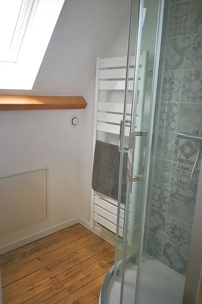 Salle de bain lumineuse au 2ᵉ étage avec lavabo sur colonne, douche moderne, fenêtre à vitrage dépoli et sol en bois, gîte Bouteille à la Mer, Côte d’Opale, Gravelines.