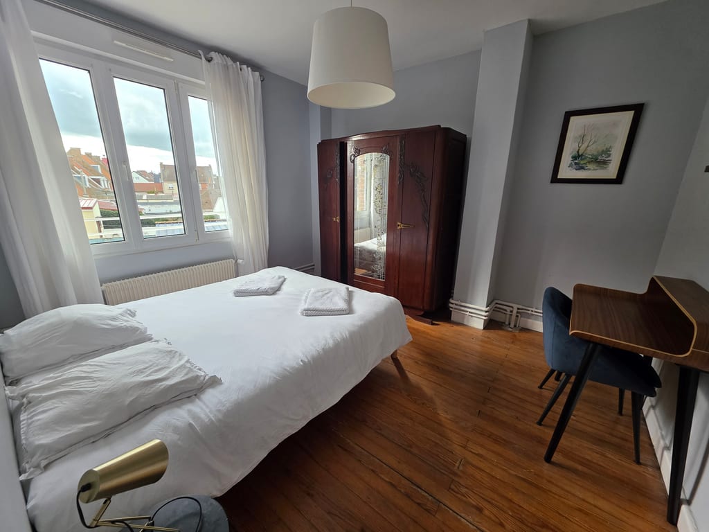 Chambre double lumineuse côté jardin avec parquet ancien, armoire en bois et petit coin bureau, idéale pour des vacances famille littoral Nord.