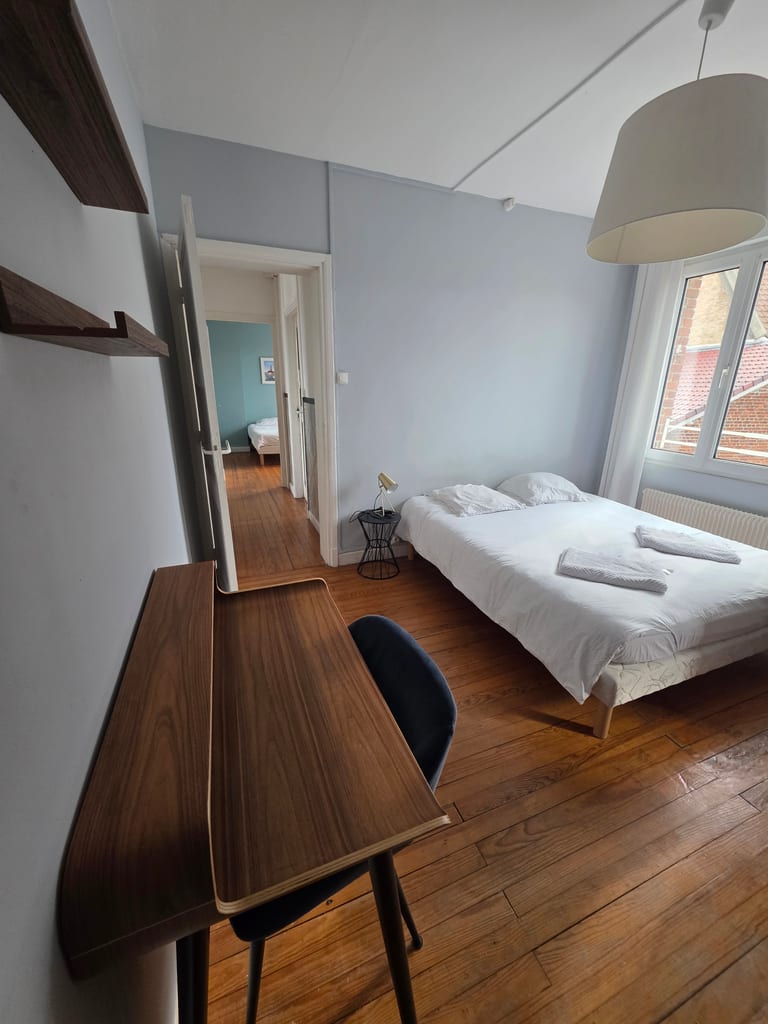 Chambre lumineuse avec lit double, parquet en bois et bureau, offrant une vue sur le jardin. Un espace idéal pour une location saisonnière à Grand-Fort-Philippe.