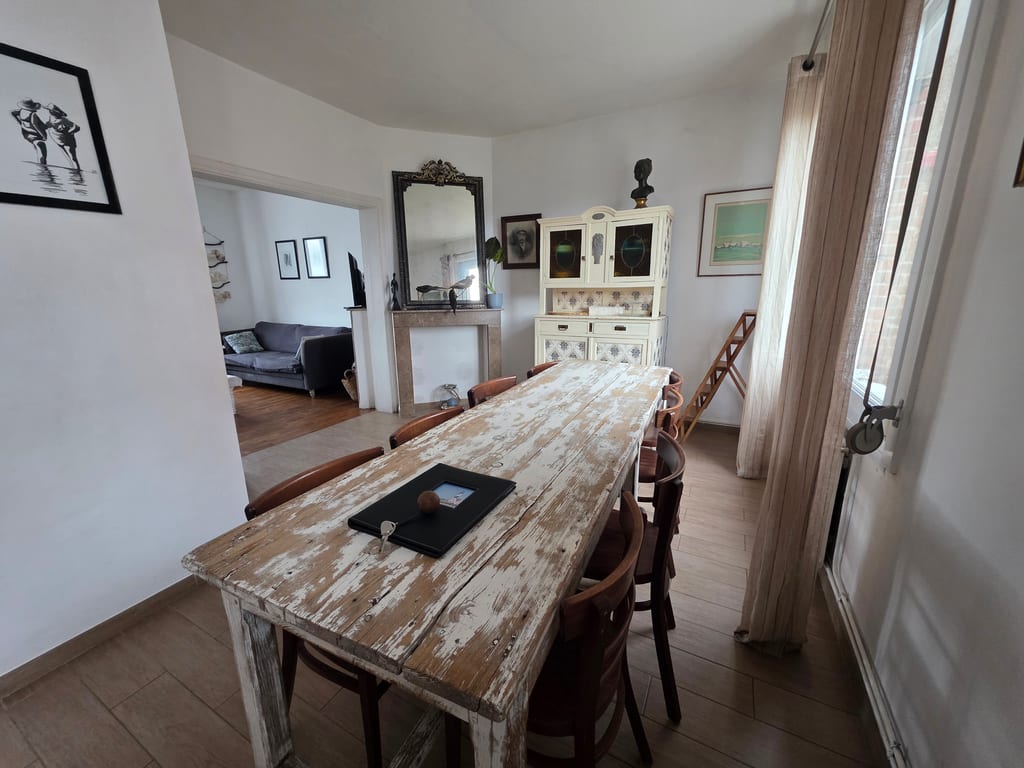 aste salle à manger lumineuse avec une longue table en bois patiné, des chaises bistrot et un buffet vintage dans notre gîte proche plage Gravelines.