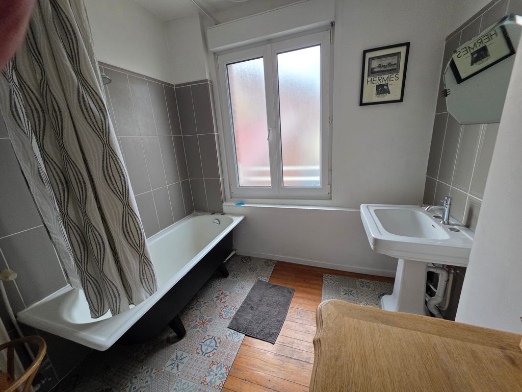 Salle de bain lumineuse avec parquet en bois, carreaux de ciment et baignoire sur pieds rétro. Un espace de détente parfait pour votre location vacances Côte d'Opale.