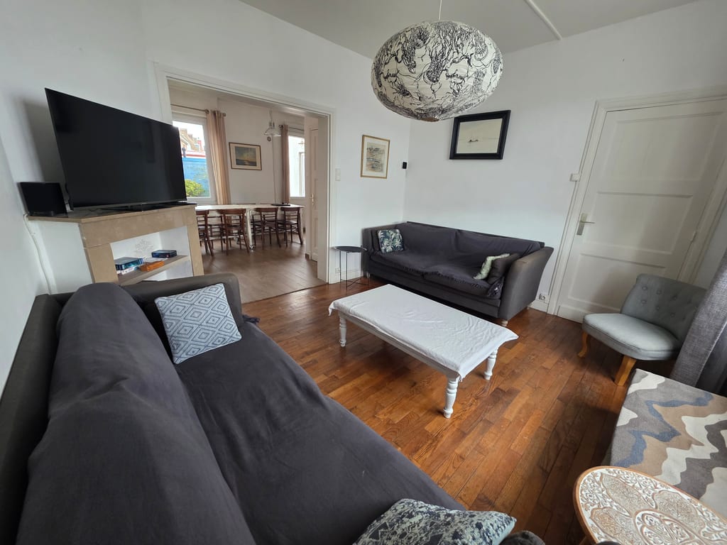 Espace salon avec télévision, grands canapés et ouverture sur la salle à manger dans notre location saisonnière à Grand-Fort-Philippe. Idéal pour se reposer en famille.
