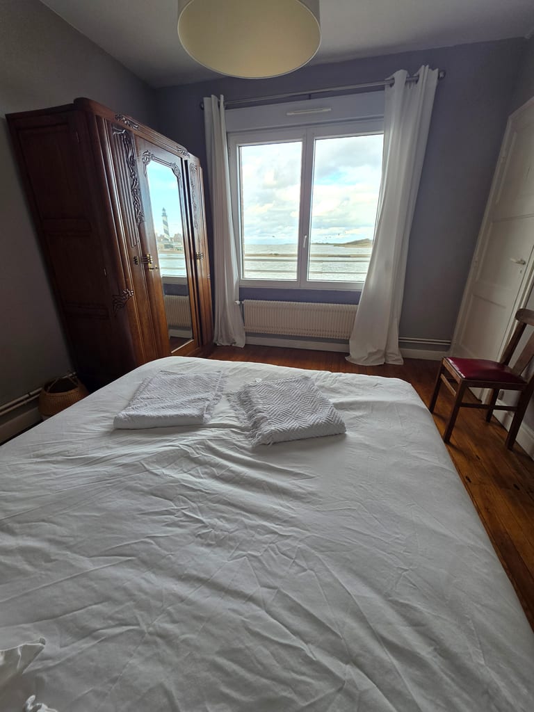 Seconde chambre double avec parquet ancien et une grande armoire à glace reflétant le phare de Petit-Fort-Philippe, idéale pour un hébergement Dunkerque bord de mer.