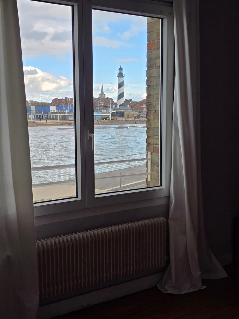 Vue depuis la fenêtre d'une chambre sur le chenal et le célèbre phare aux spirales noires et blanches, idéal pour un hébergement Dunkerque bord de mer.