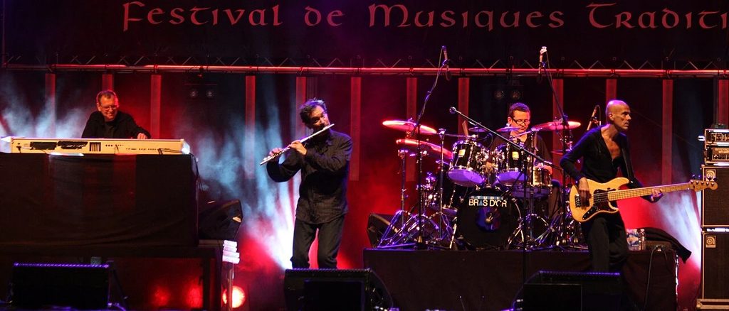 Groupe de musiciens jouant sur la scène illuminée du festival de musiques traditionnelles Het Lindeboom, une sortie festive proche de notre gîte Gravelines.